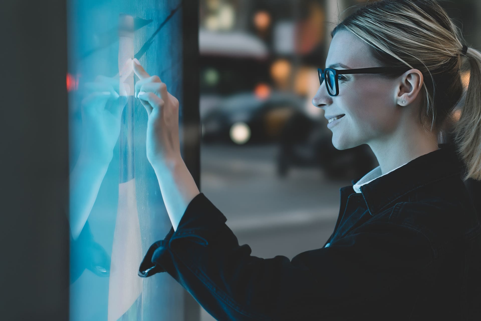 Smiling female standing at big display with advanced digital tec A woman with glasses