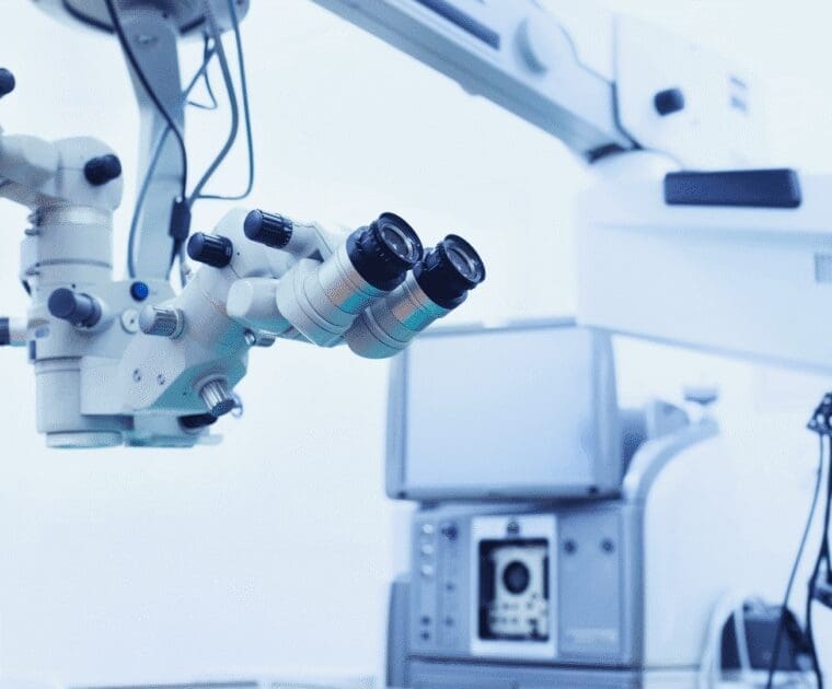 Close-up of a surgical microscope and medical equipment in a modern operating room, with a blue-tinted, sterile environment.