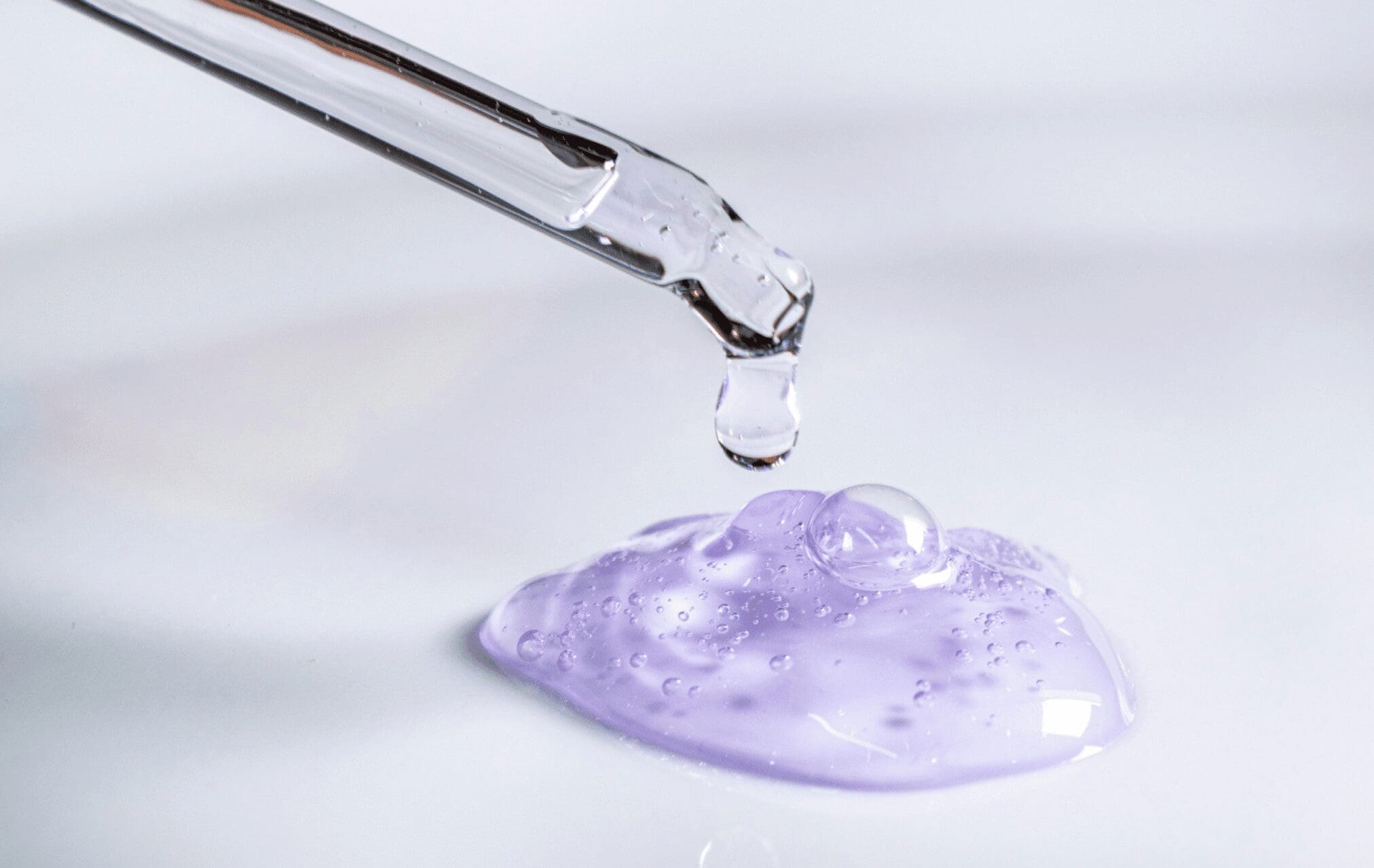 Glass pipette dropping purple serum gel on a smooth white surface