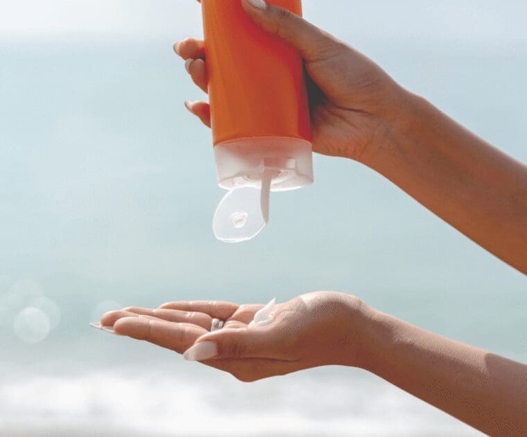 Close-up of hands squeezing sunscreen lotion from an orange bottle onto the palm at the beach