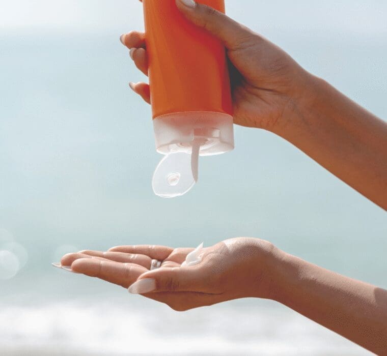Close-up of hands squeezing sunscreen lotion from an orange bottle onto the palm at the beach