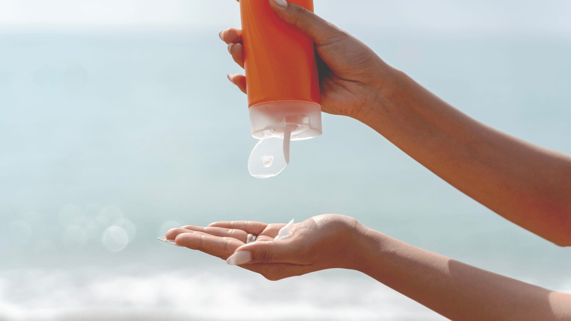 Close-up of hands squeezing sunscreen lotion from an orange bottle onto the palm at the beach