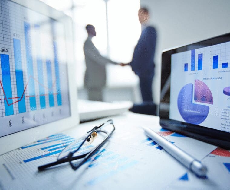 Business charts and analytics dashboards on screens with two professionals shaking hands in the background.