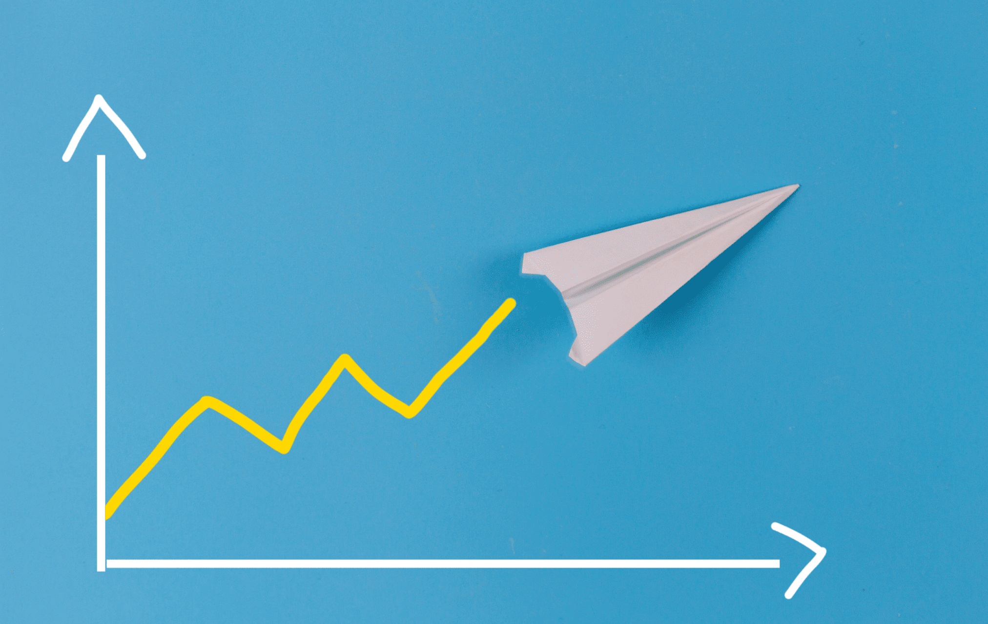 Paper airplane flying upward alongside a yellow growth line on a blue background, symbolizing business success.