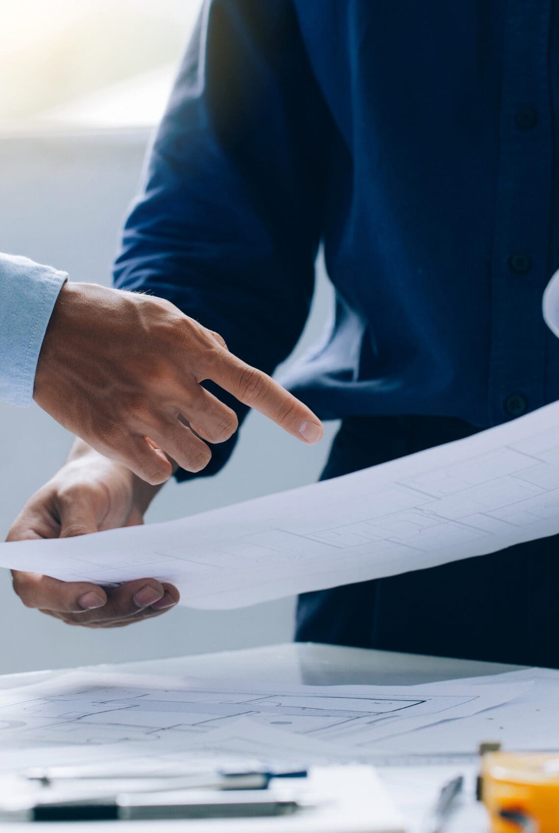 Two professionals reviewing technical drawings and discussing project details at a desk.