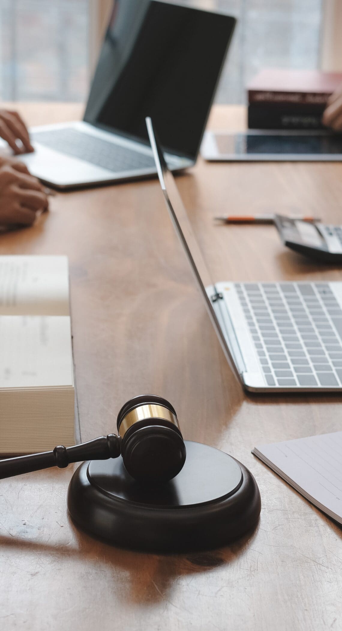 Legal professionals reviewing documents with laptops and a gavel on the table during a compliance meeting.