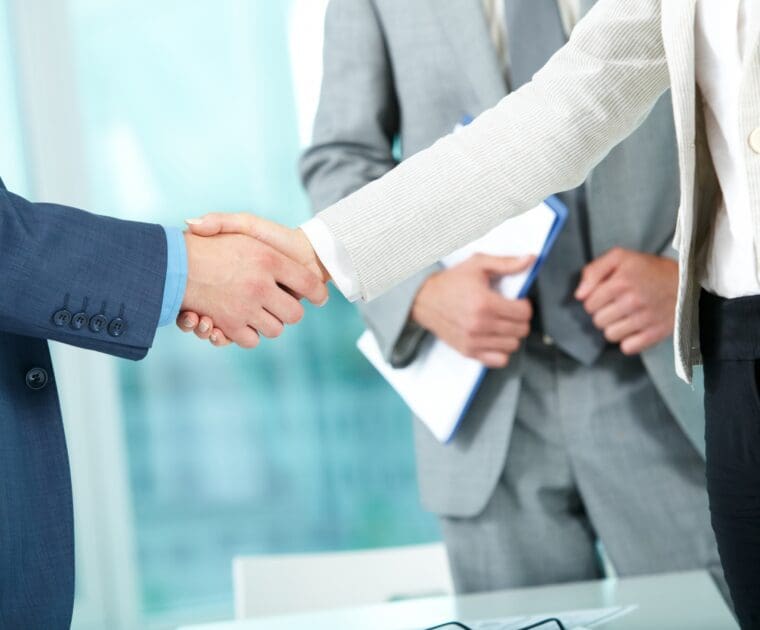 Business professionals shaking hands during a regulatory consulting and compliance partnership meeting.